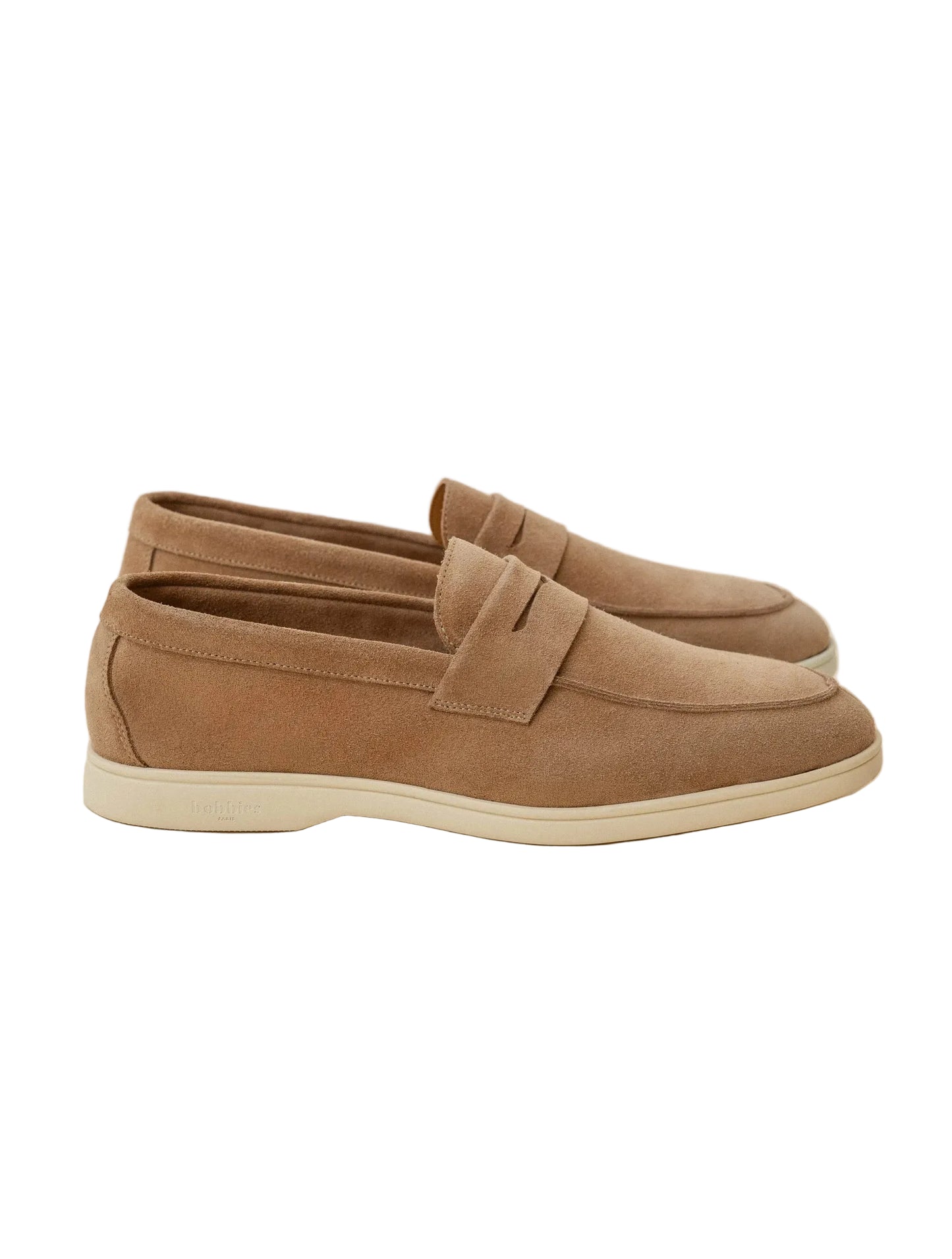 A pair of taupe-brown suede penny loafers with off-white soles, displayed on a clean, light beige background.